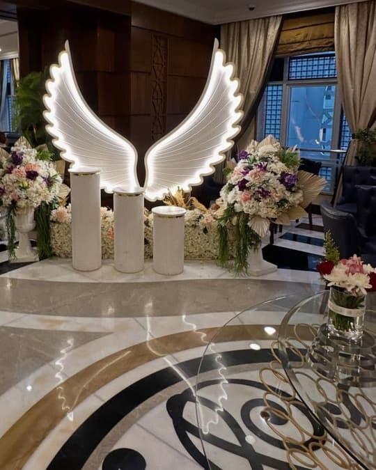مدخل بجناحين أبيضين مضيئين وتنسيقات ورد على الجانبين في قاعة فندق